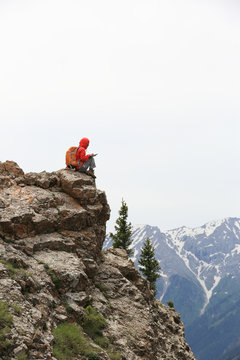 woman backpacker use digital tablet on mountain peak cliff