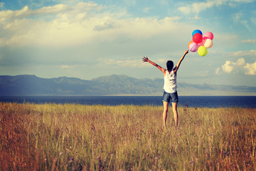 cheering young asian woman on grassland with colored balloons
