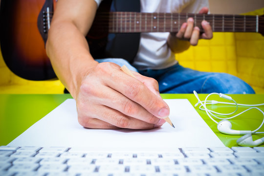 Asian Professional Composer Hands Writing Songs On White Paper With Acoustic Guitar & Computer