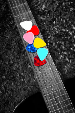 vertical photo of colourful picks on acoustic guitar fingerboard for music background