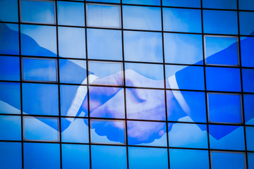 businessman handshake with cloud and sky reflection on glass windows building