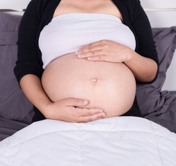 close up belly of pregnant woman sitting on bed in the bedroom