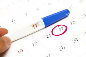 Pregnancy test with positive result lying on calendar