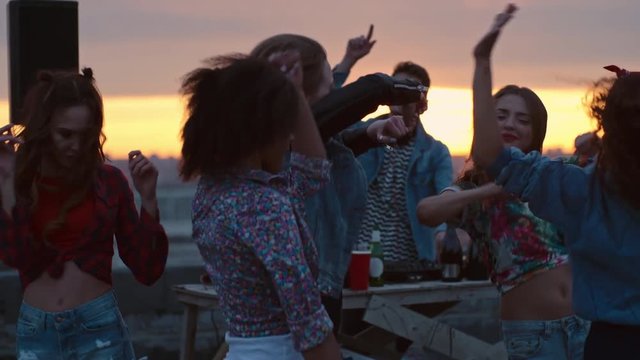 Group of young multi-ethnic people dancing energetically to the music played by dj at rooftop party at sunset