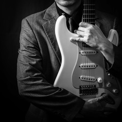 male musician in grey suit holding electric guitar on dark background