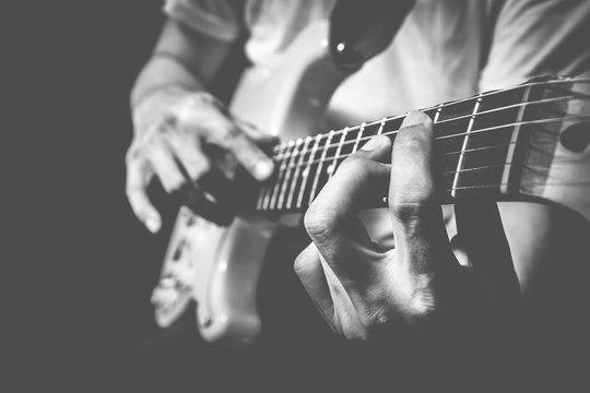closeup male musician hands playing electric guitar on stage + bw film filter
