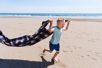 Shot of a little boy running while holding a blanket on a beach