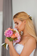 Obraz na płótnie Canvas Portrait of a beautiful blonde bride with bouquet in an interior light, wedding concept