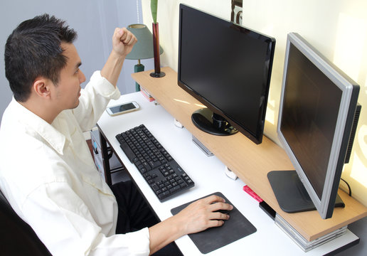 Asian handsome businessman work in front of dual monitors computer and glad successful