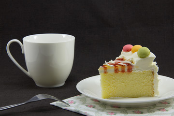 a piece of butter cake on white plate with a fork and a cup on black textile background, selective focus