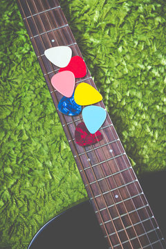 vertical photo of colourful picks on acoustic guitar fingerboard