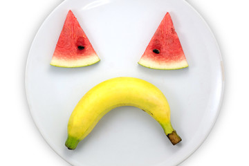 Watermelon slice and banana sad faces on white plate on white background , concept enjoy eating.