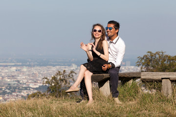 Elegant multiethnic couple sitting on a bench in European countryside