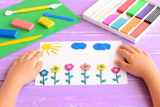 Child shows a card with plasticine flowers, sun and clouds. Supplies for children art crafts on a wooden table. Modeling clay crafts idea for kids. Activity in kindergarten and at home 
