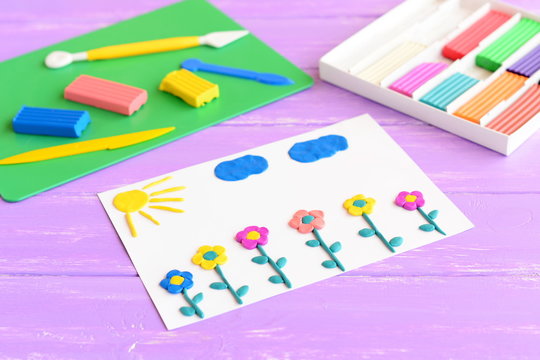 Card with plasticine flowers, sun and clouds. Plasticine set on a wooden table. Children modeling clay art. Crafts idea for development of fine motor skills in children