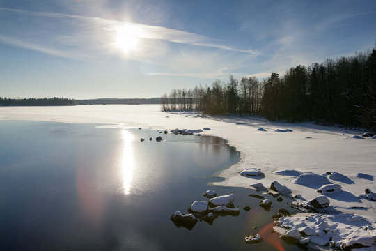 A wintry landscape in Finland during a sunny day in the winter. Image taken in February. The sun is reflecting from the water. Flare effect added.