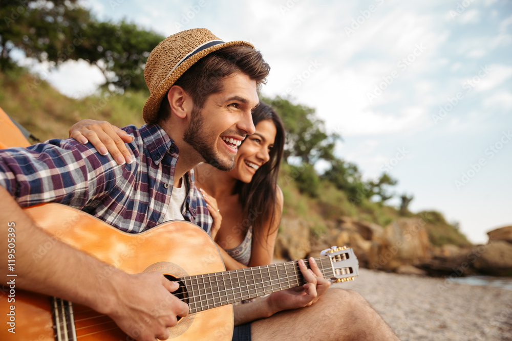 Poster man playing guitar for his girlfriend sitting at the tent