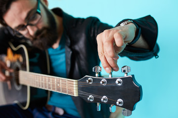 Bearded hipster man hand adjusting on acoustic guitar.