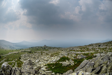 Summer cloudy day in the mountains. Huge stone in the grass.