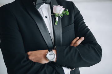 The groom is wearing a black suit with clock on the hand, with the buttonhole of pink flowers and greenery