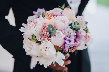 The groom holds a wedding bouquet of pink and white flowers with greenery