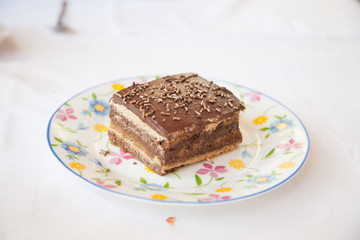 square piece of brown chocolate cake on white circle ceramic dish with flowers on white tablecloth
