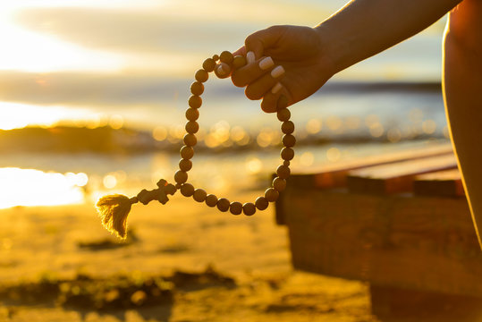 silhouette of the rosary in female hands on a sunset background,