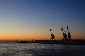 Obraz premium SEA PORT OF GDYNIA AT DAWN. Cloudless sky, harbor cranes and a quay at the port of Gdynia at dawn
