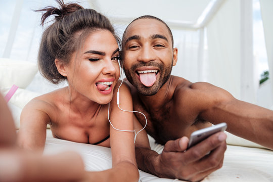 Cheerful couple making selfie and showing tongues at the beach