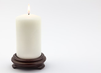 Single white lit candle on white background