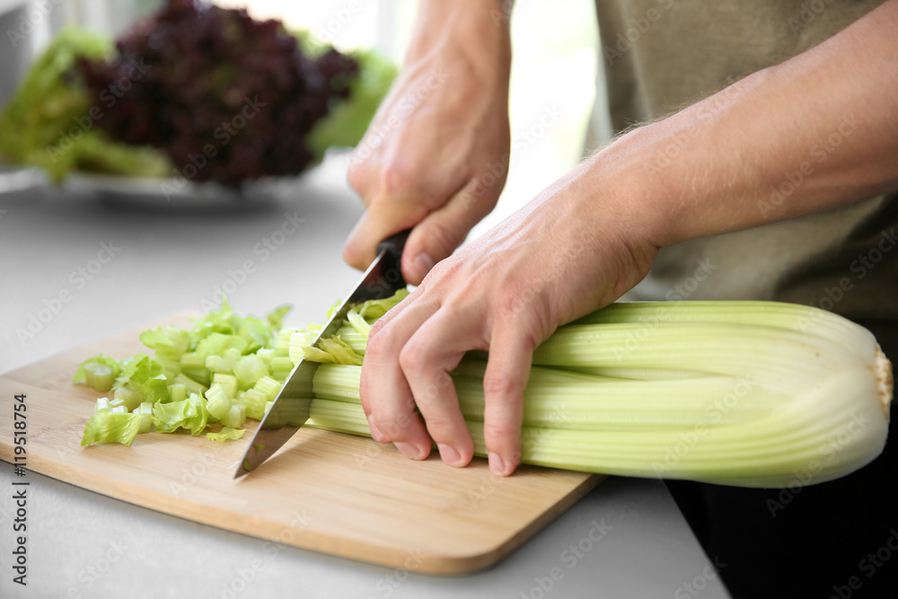 Poster Male hands cutting celery on wooden board closeup