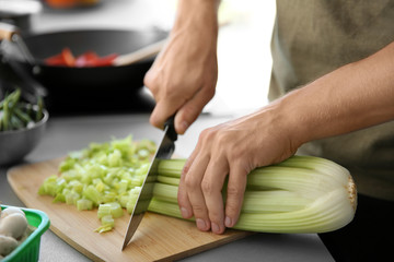 Male hands cutting celery on wooden board closeup