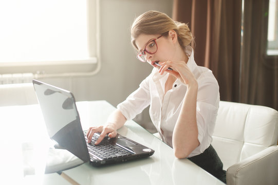 Portrait of a casual young businesswoman in blouse using laptop computer in office. The sunlight in the window.
