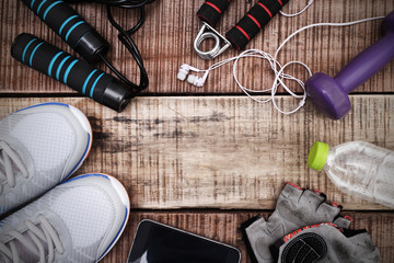 Fototapeta na wymiar Sports equipment - sneakers, skipping rope, dumbbells, smartphone and headphones. Sport background on wooden floor, top view.