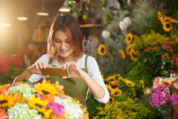 Asian young woman using smartphone to take photo of flowers