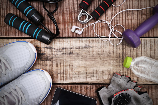 Sports equipment - sneakers, skipping rope, dumbbells, smartphone and headphones. Sport background on wooden floor, top view.