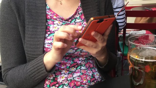 Zoom In Girl Messaging On Smart Phone In a Bar. Girl sitting in a bar sending messages on a smart phone and having a beer.