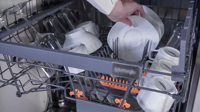 Woman is putting saucers in the dishwasher. She is placing them on the top rack. Close-up shot.
