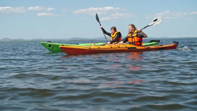 Couple of kayakers in life jackets rowing on scenic lake together
