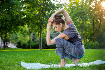 Young woman doing yoga exercises in the summer city park.