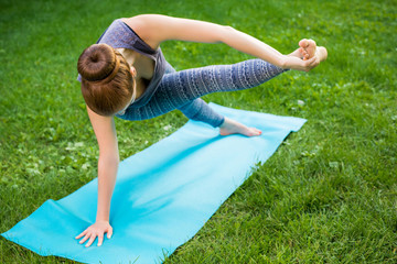 Fototapeta premium Young woman doing yoga exercises in the summer city park.