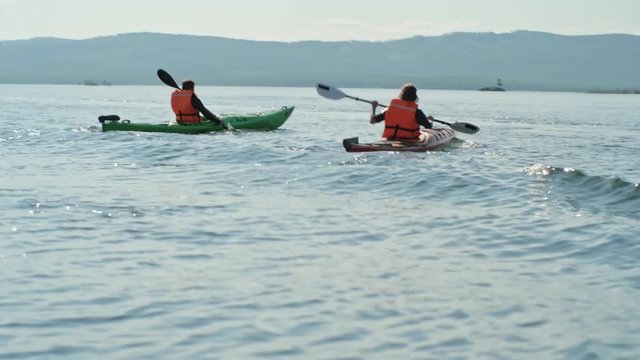Man and woman rowing kayaks on waving lake in the summer