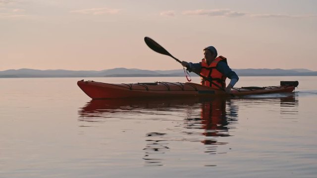 Man rowing a kayak with paddle on the lake in the evening at sunset