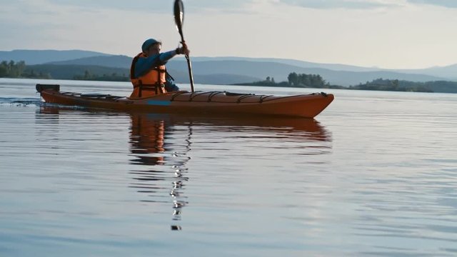 Man wearing orange life jacket while paddling a boat in the lake 