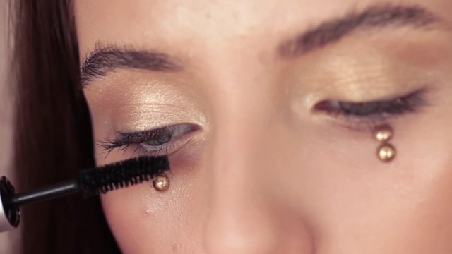 Beautiful young girl paints the eyelashes makeup