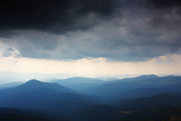 Mountain landscape. Mountain range in haze. Rays of light in lumen of mountains and clouds. Stormy weather. Panorama