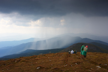 Tourists on top of mountain. Group of people relax and enjoy beautiful panorama of mountain ranges. Wall of rain under stormy sky. Rainy weather. Panorama.