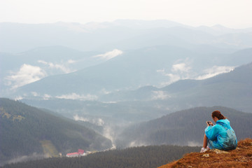 Girl with mobile phone on top of mountain. Mobile telephony, fast Internet in mountains. Chat on phone. Mountain landscape. Rain clouds, dramatic mood