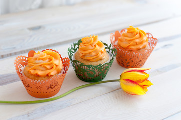 Three delicious cupcakes with orange cream and orange tulips