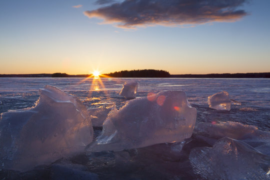 Small ice blocks on the lake during sunset. An image of partly melted ice particles laying on the ice. A colorful sunset is in the background. Image taken from low point of view.